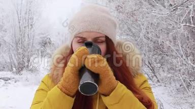 年轻的红发女孩戴着一顶温<strong>暖</strong>的针织帽子和一件黄色的<strong>冬季</strong>夹克，在金属杯上喝一杯热饮料。